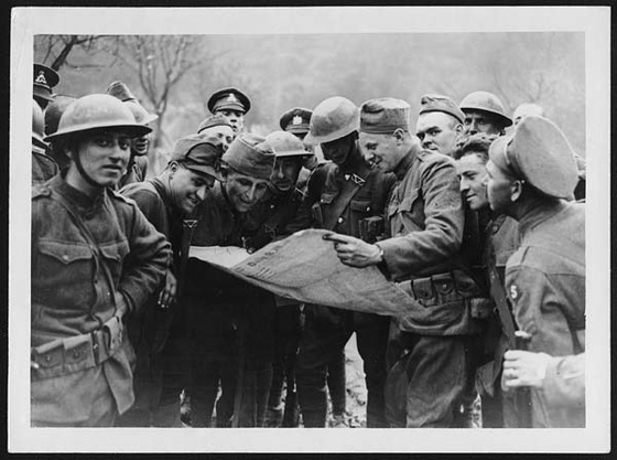 American and British soldiers gathered around, looking at a news